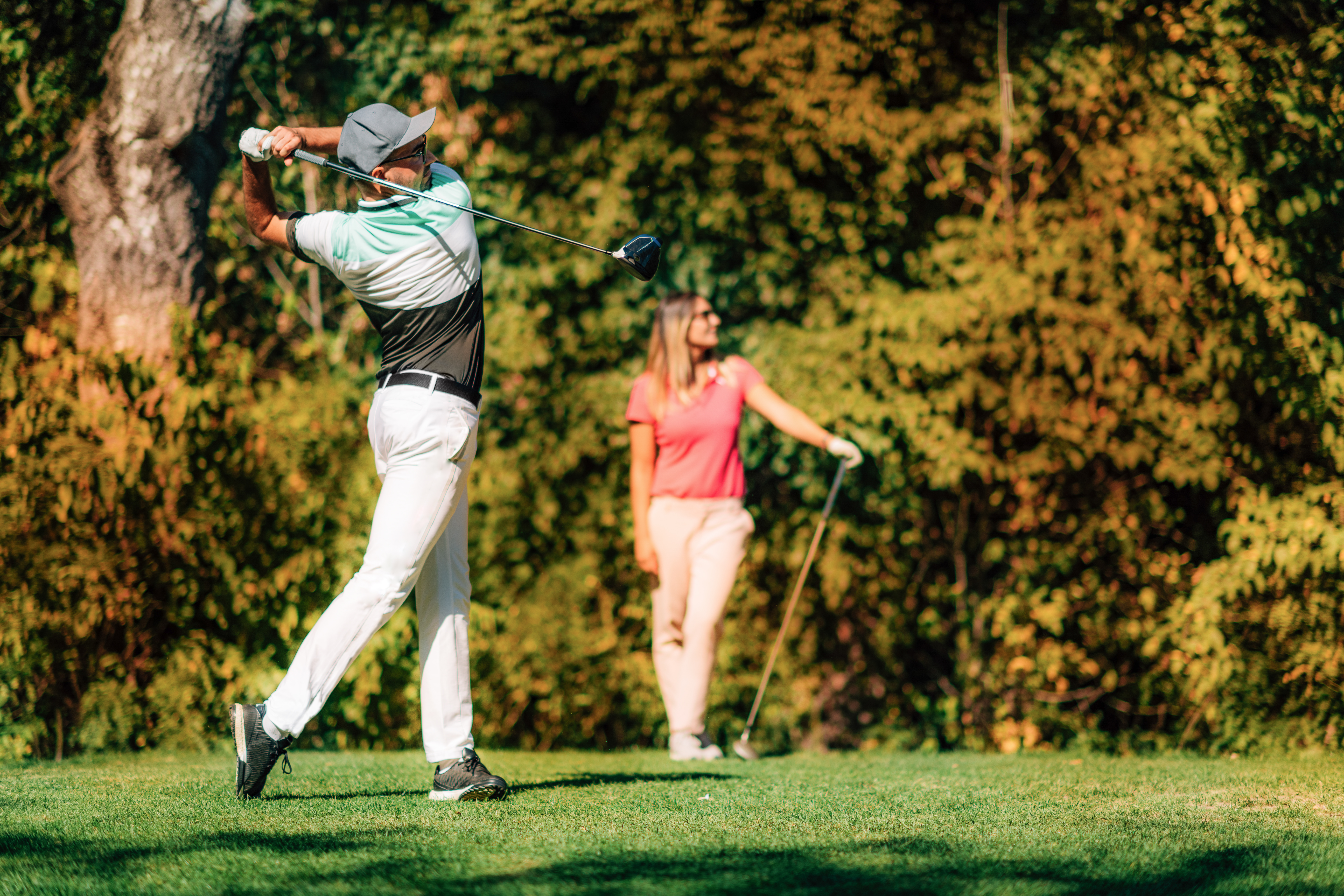 Golfing couple. Man in the swing position, lady following the ball in flight