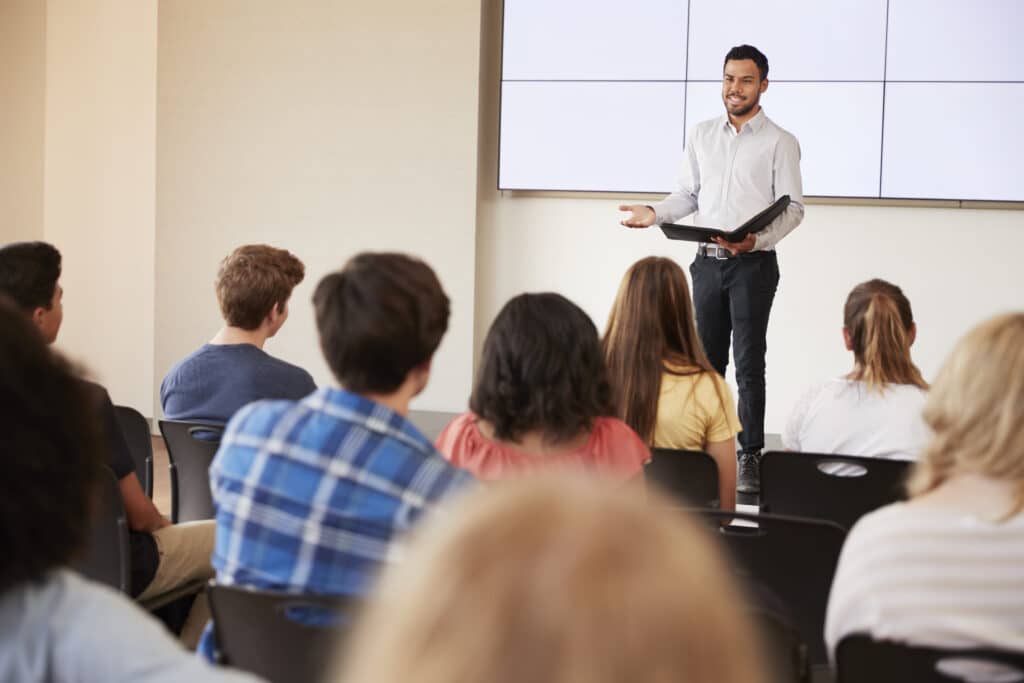 Teacher Giving Presentation To High School Class In Front Of Screen