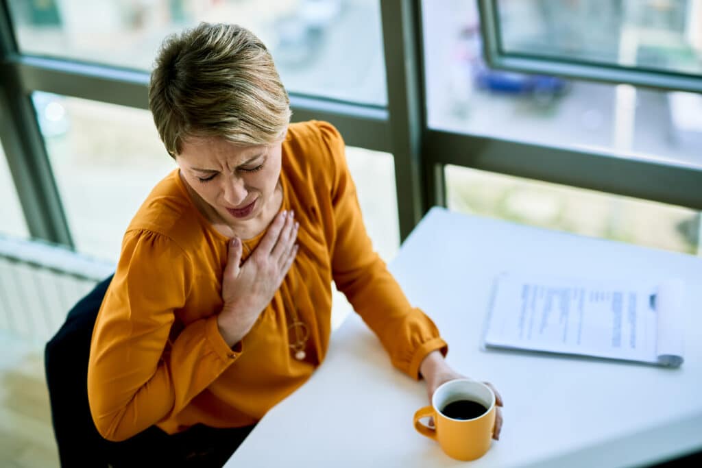 High angle view of businesswoman coughing while having coffee break in the office.